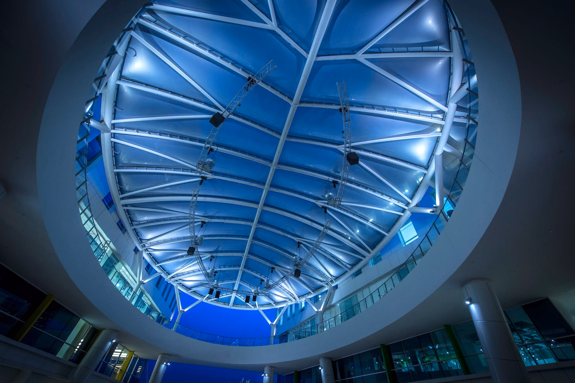 Looking up through a circular opening to an uplit leaf-shaped fabric canopy at blue hour