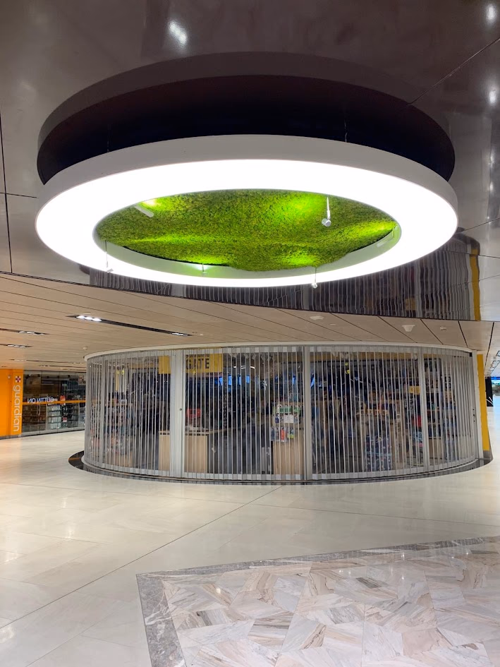 Terminal concourse with a large illuminated ring suspended over a planted feature above a circular shopfront