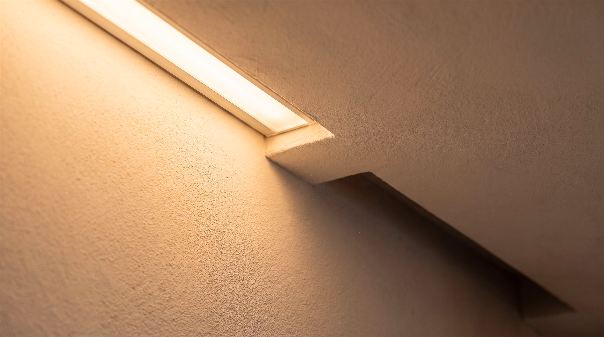 Close detail of a recessed linear cove fixture glowing warm against fine plaster texture