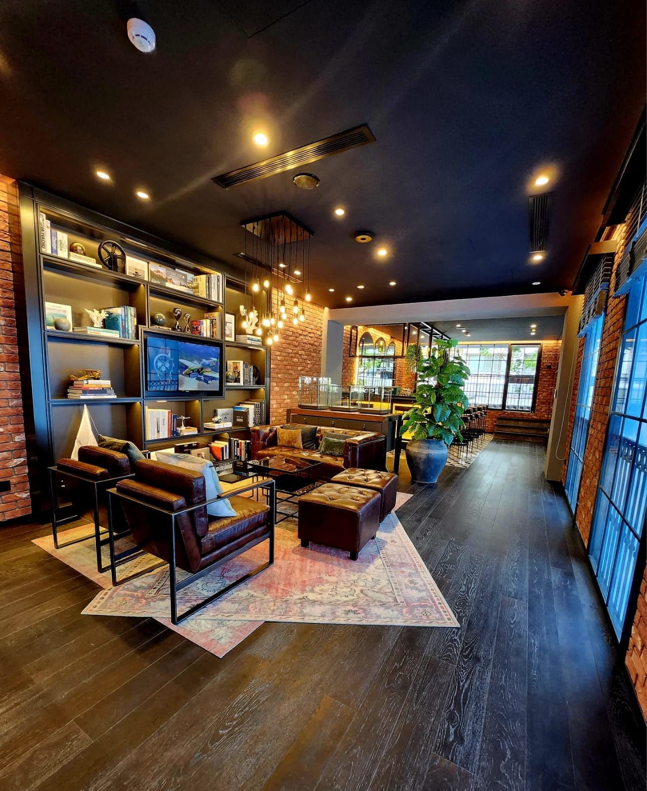 Boutique lounge seen from the entrance, with lit bookshelves, a filament pendant cluster and downlights along a dark ceiling