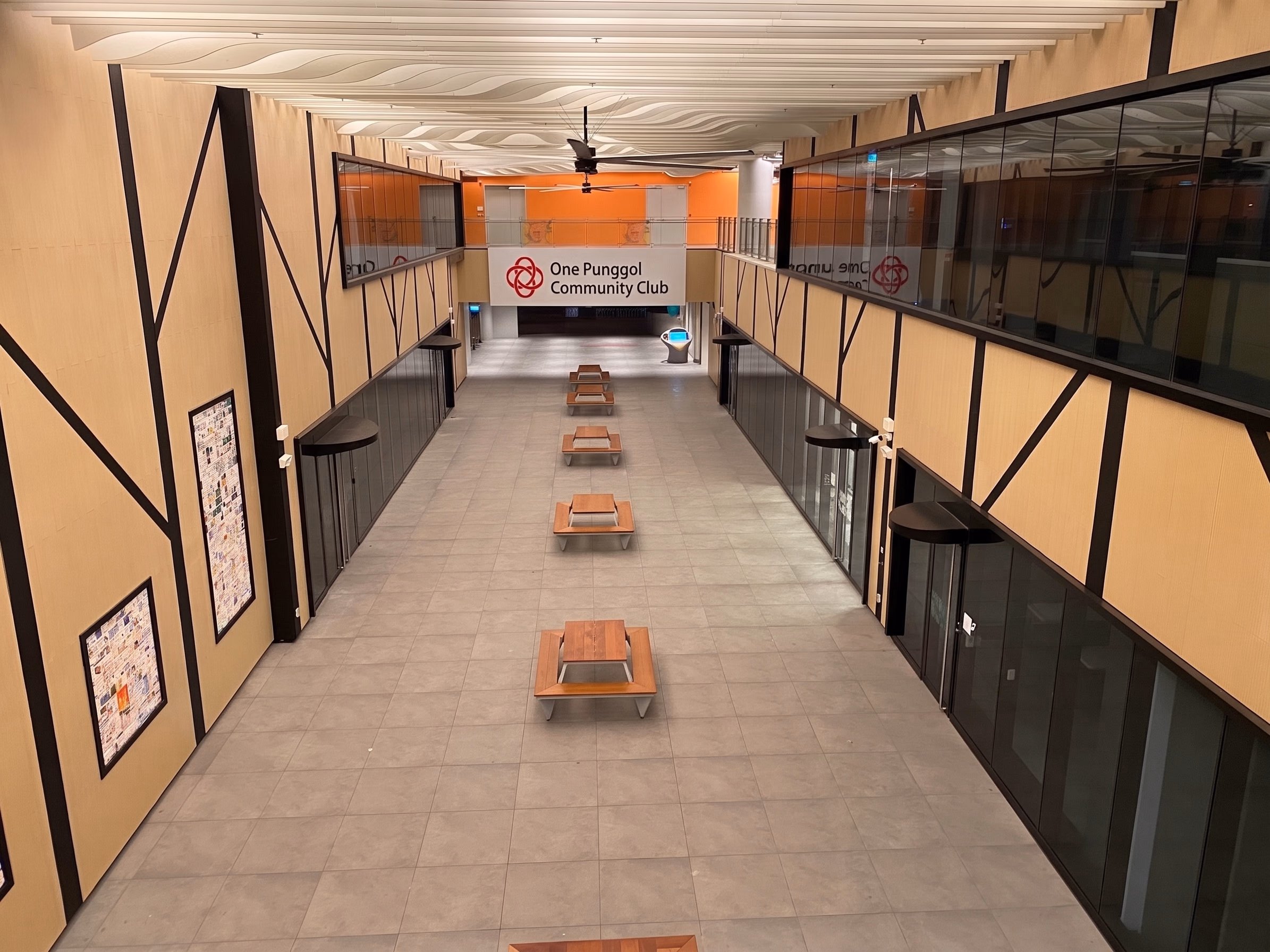 Double-height internal street in a community club, lit by continuous ceiling slots along timber-framed walls