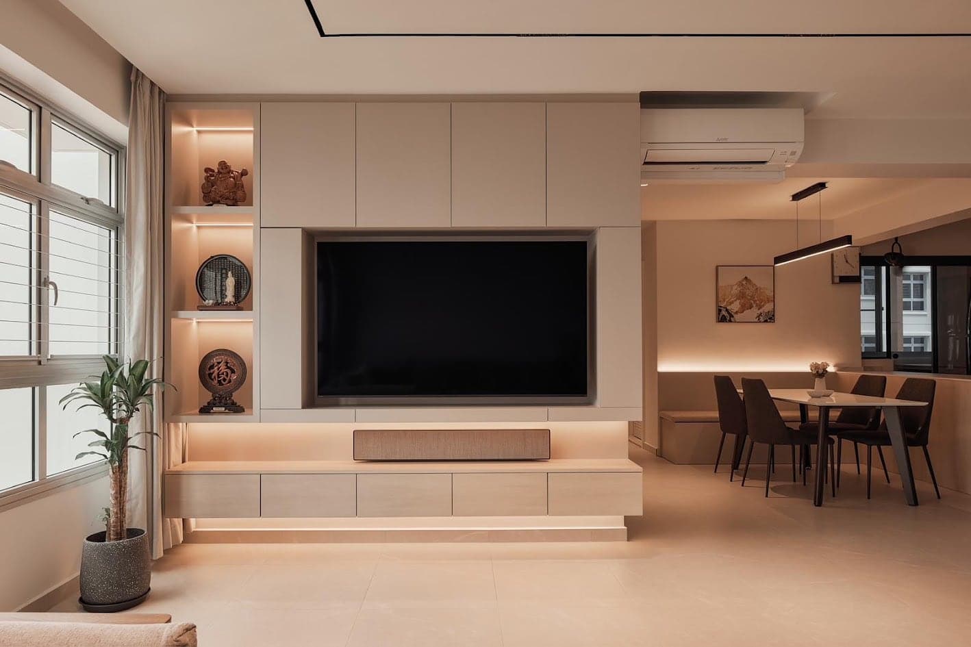 Living and dining room with a built-in media wall, warm concealed lighting under the cabinets and in the display niches, and a linear pendant over the dining table