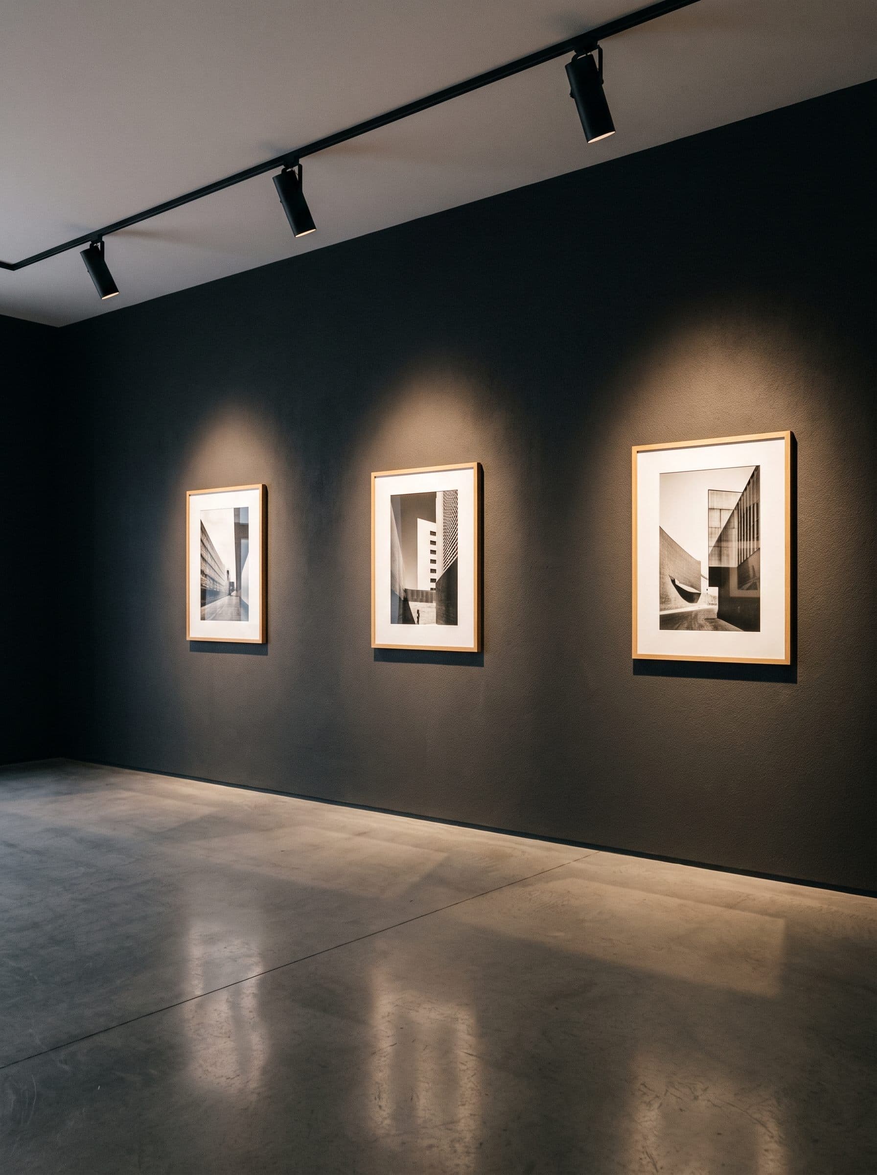 Track spotlights washing a dark gallery wall hung with framed architectural photographs